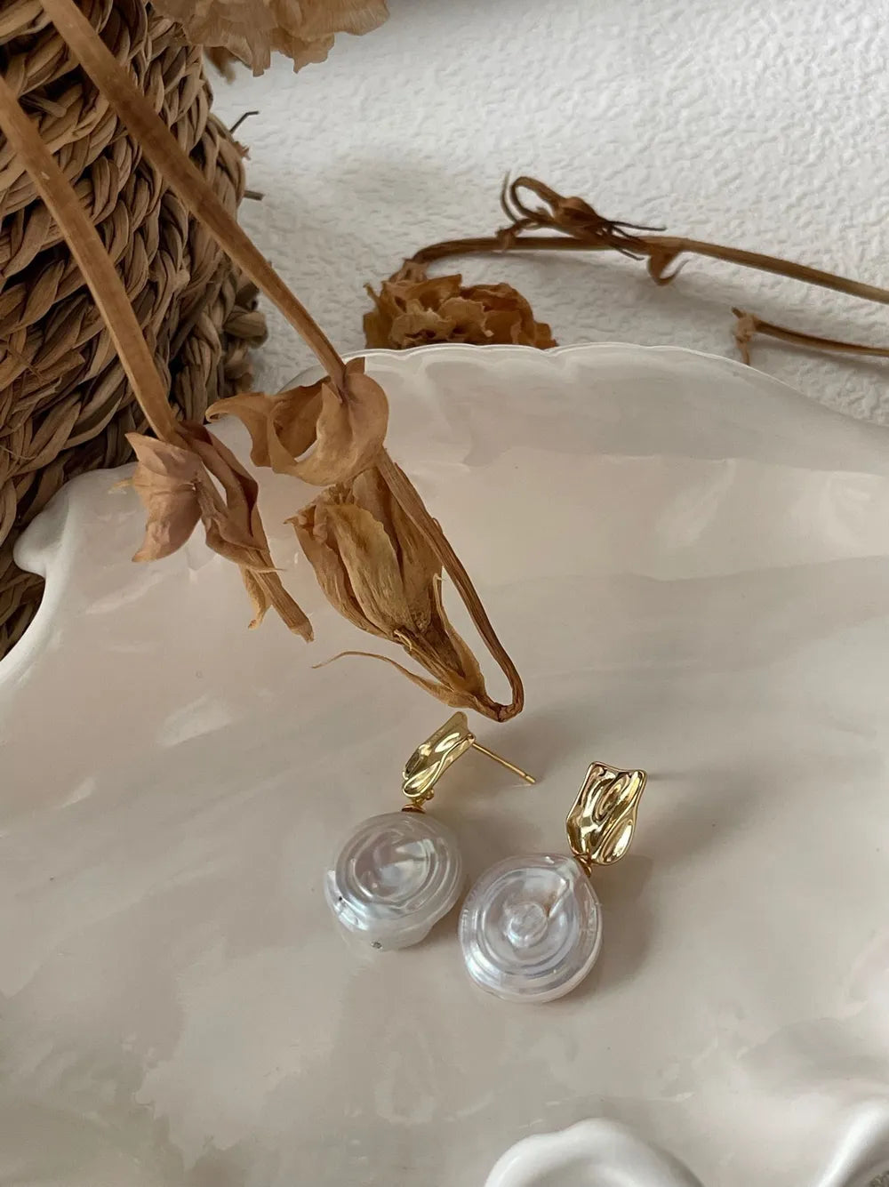 Pair of coin baroque pearl drop earrings on white textured backdrop showing metallic shine.
