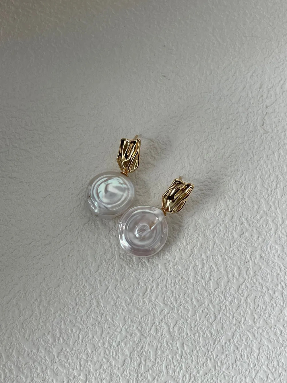 Coin baroque pearl drop earrings resting on textured background showing post backing detail.