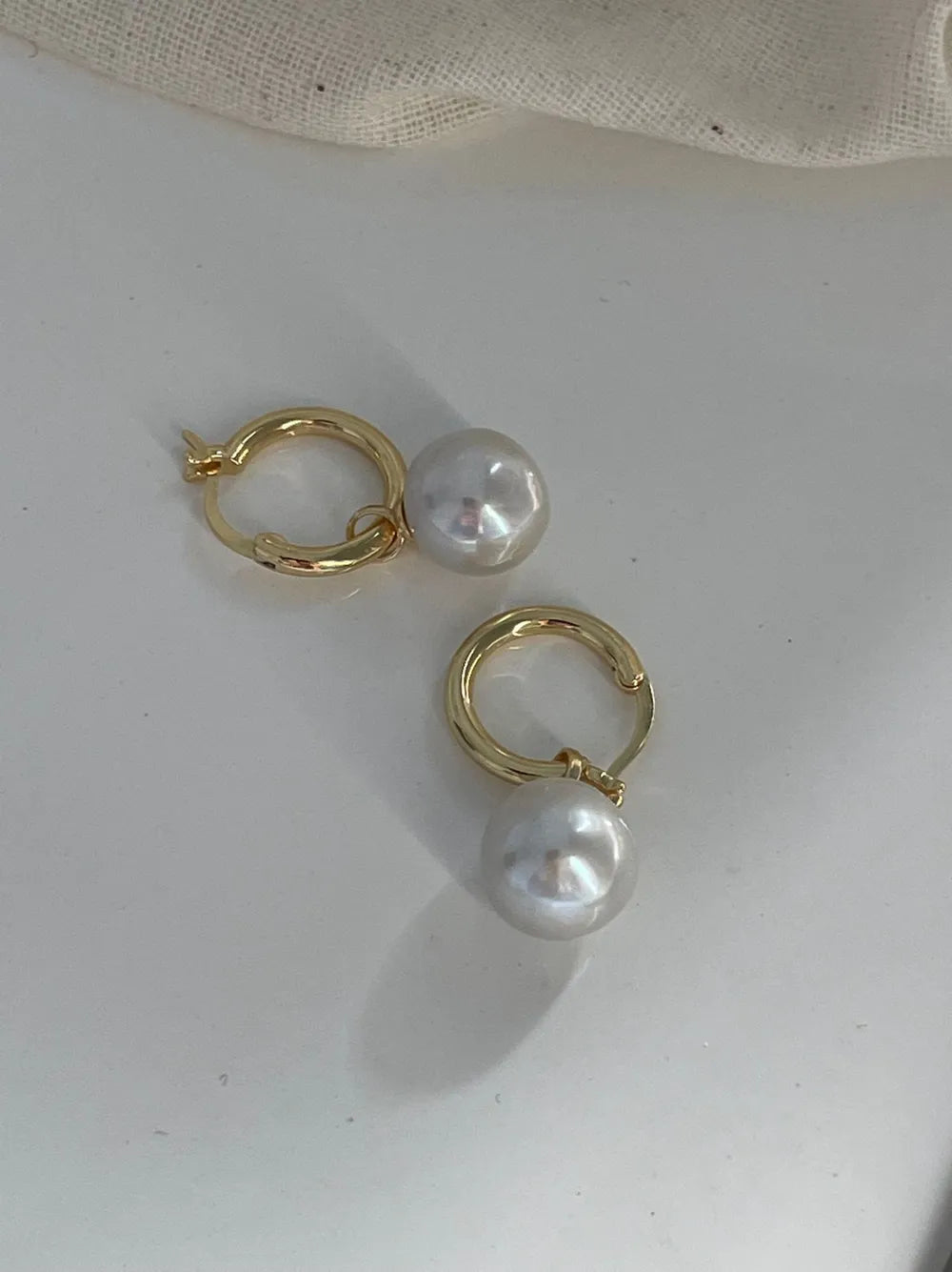 Overhead view of the crystal baroque pearl hoop earrings resting on a white smooth surface.