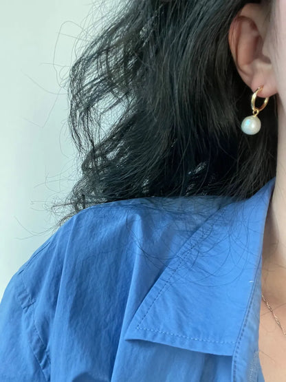 Model wearing the crystal baroque pearl huggie hoop earring paired with a blue shirt.