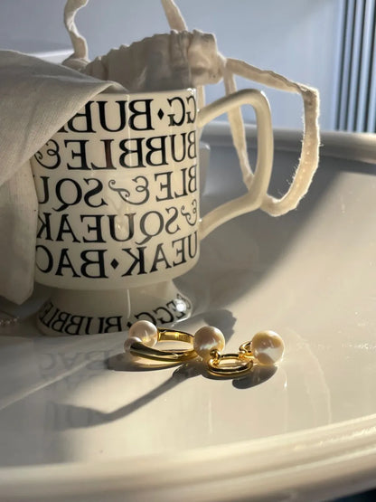 Crystal baroque pearl huggie earrings and matching S925 gold pearl ring under warm sunlight on beige tableware.