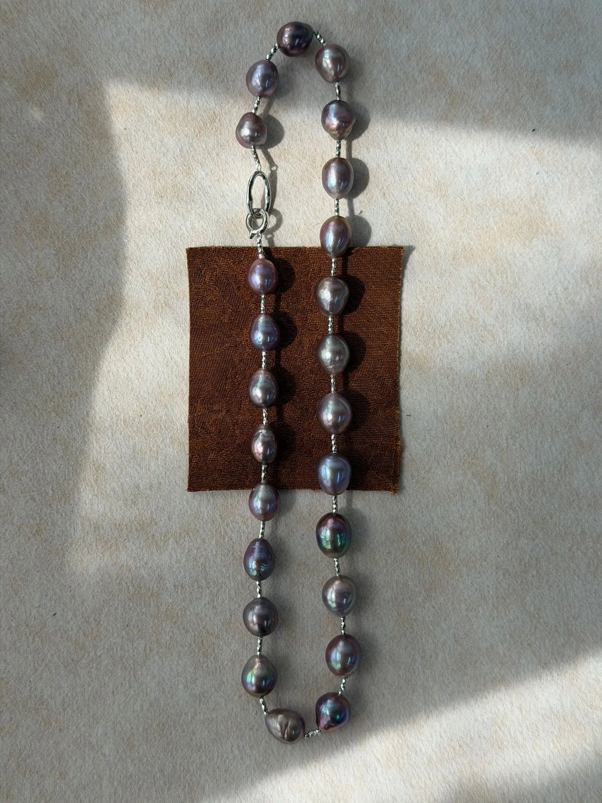 Dark purple baroque pearl necklace folded over a brown velvet fabric prop under natural light.