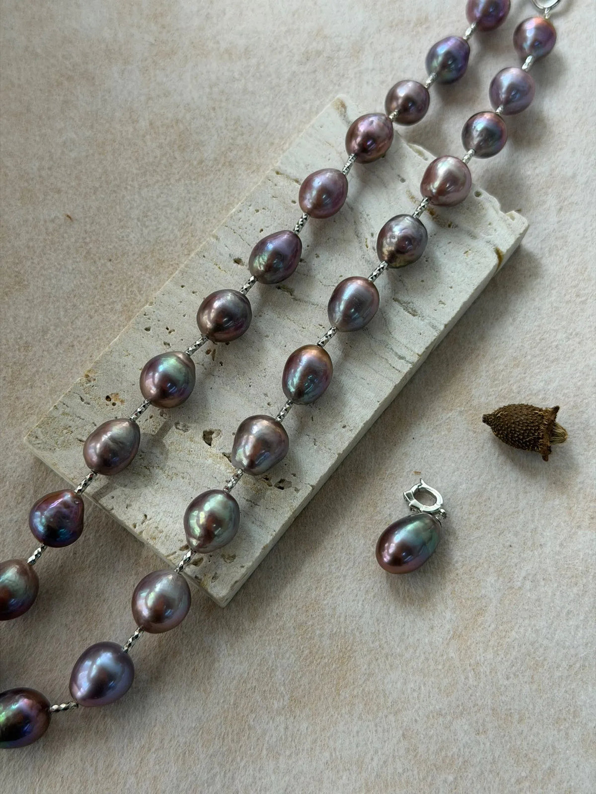 Flatlay view of blue-violet baroque pearl strand on stone board showing the detached pearl drop pendant separately.