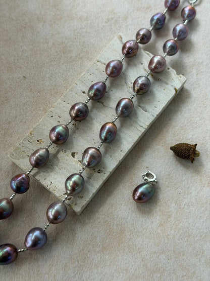 Flatlay view of blue-violet baroque pearl strand on stone board showing the detached pearl drop pendant separately.