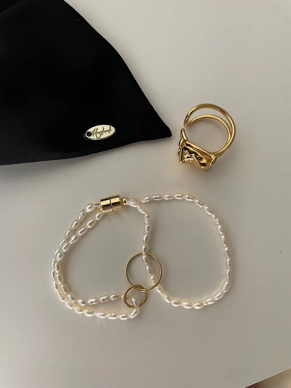 Double circle seed pearl layered bracelet with 18k gold hardware displayed next to a gold ring on beige tabletop.