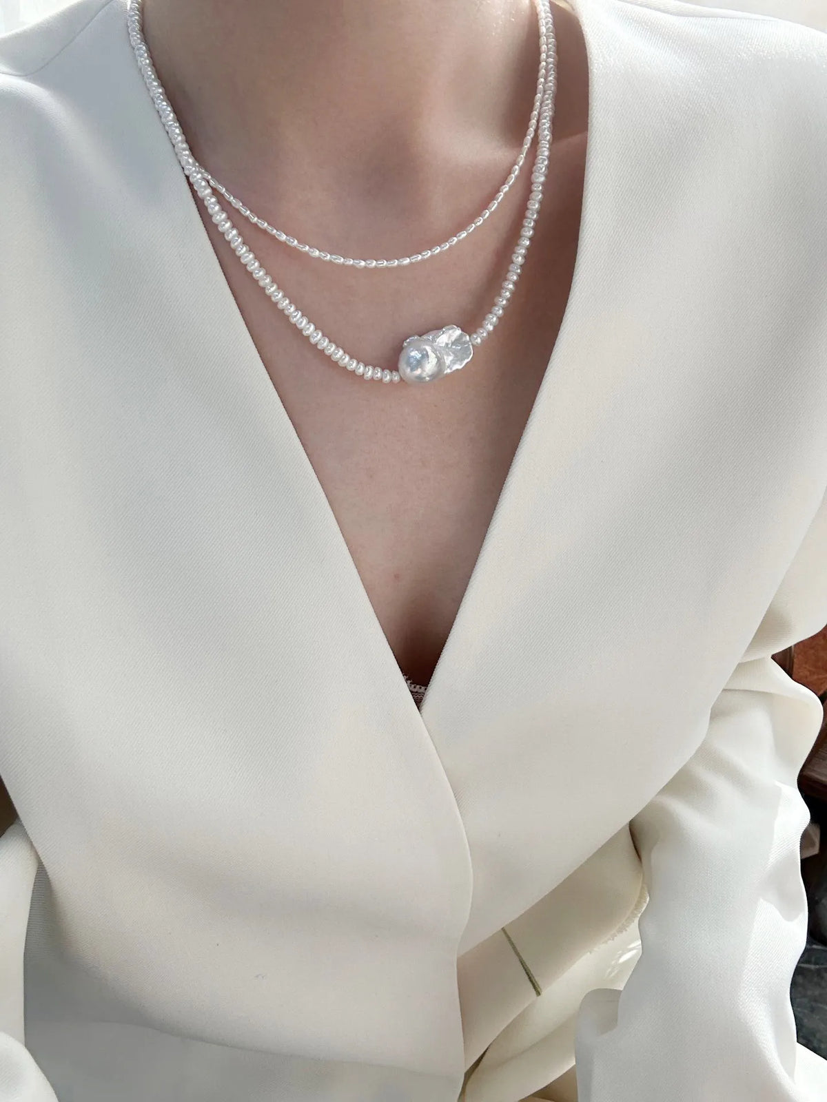 High-fashion double-layer pearl necklace look worn under a tailored white blazer.