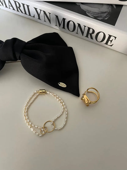 Double-strand seed pearl bracelet styled next to a black ribbon prop on white surface.