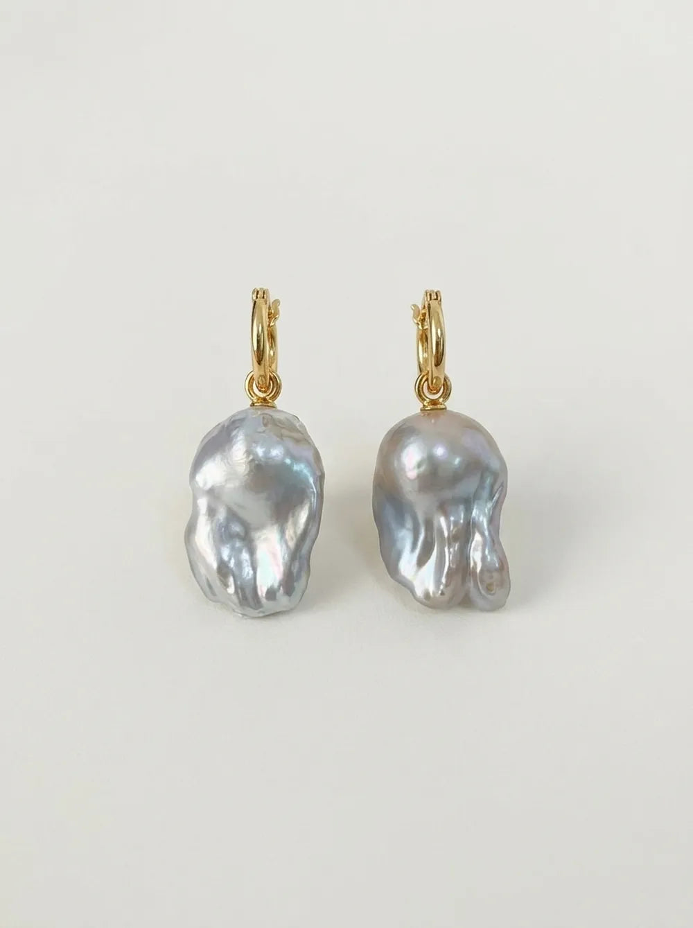 Pair of 18k gold-plated S925 sterling silver flame-tailed baroque pearl huggie hoop earrings flatlay.