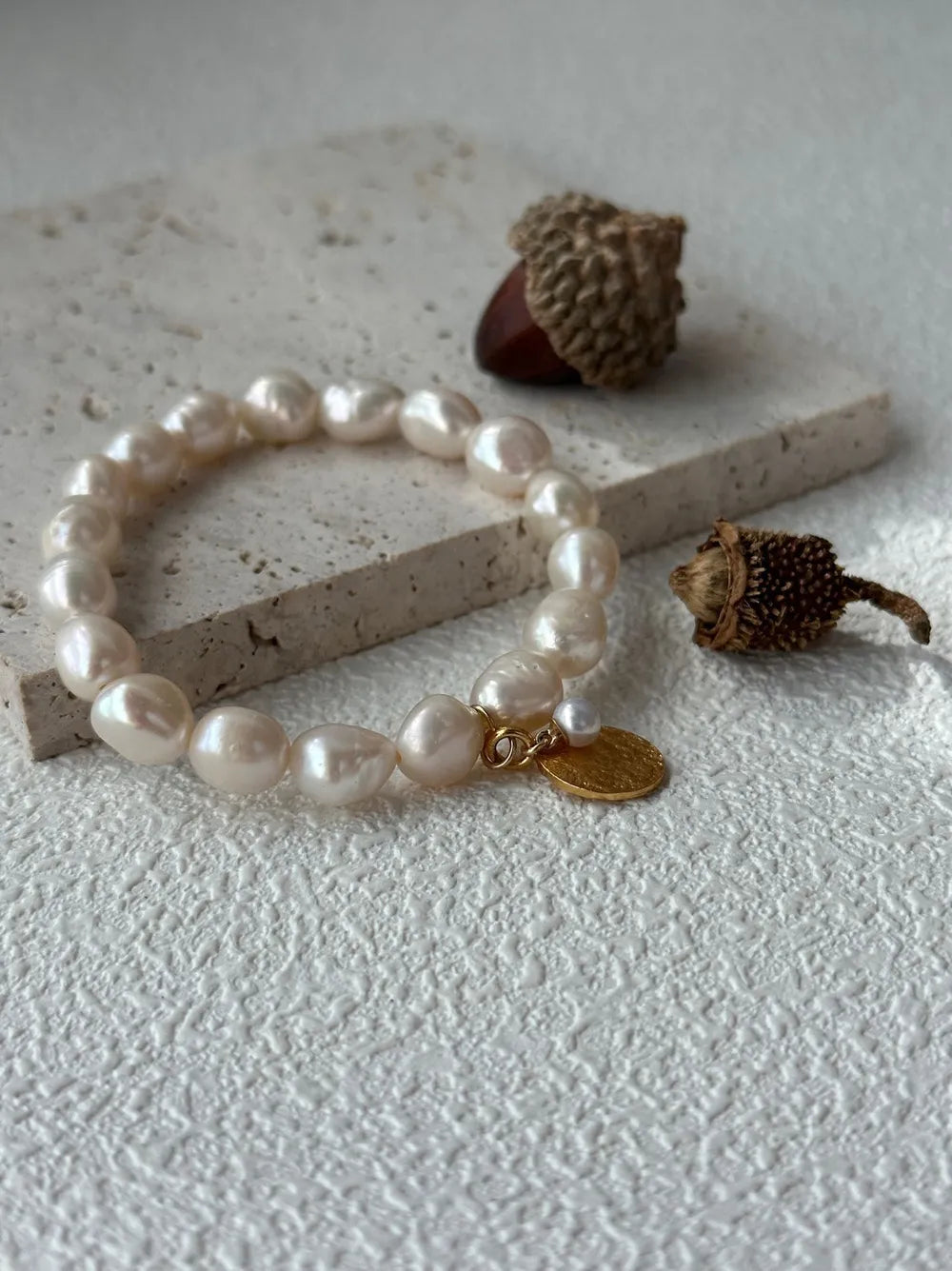 Overhead close-up shot highlighting the freshwater pearl nacre and gold coin charm next to acorn.