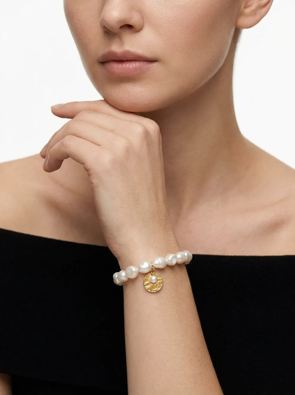 Model holding hand to chin displaying the gardener freshwater pearl elastic bracelet on wrist.