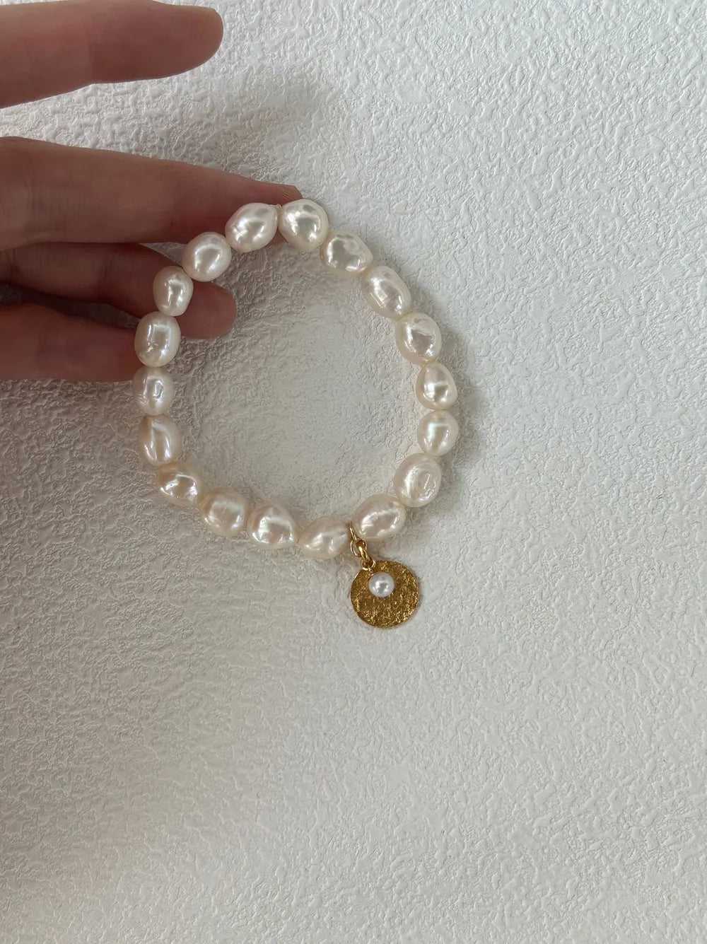 Hand holding the gardener freshwater pearl elastic bracelet showing gold coin charm.
