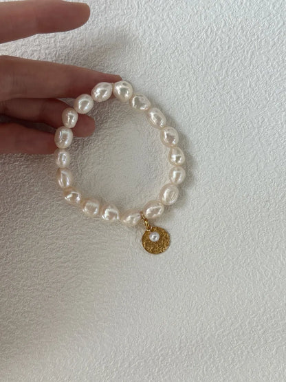 Hand holding the gardener freshwater pearl elastic bracelet showing gold coin charm.