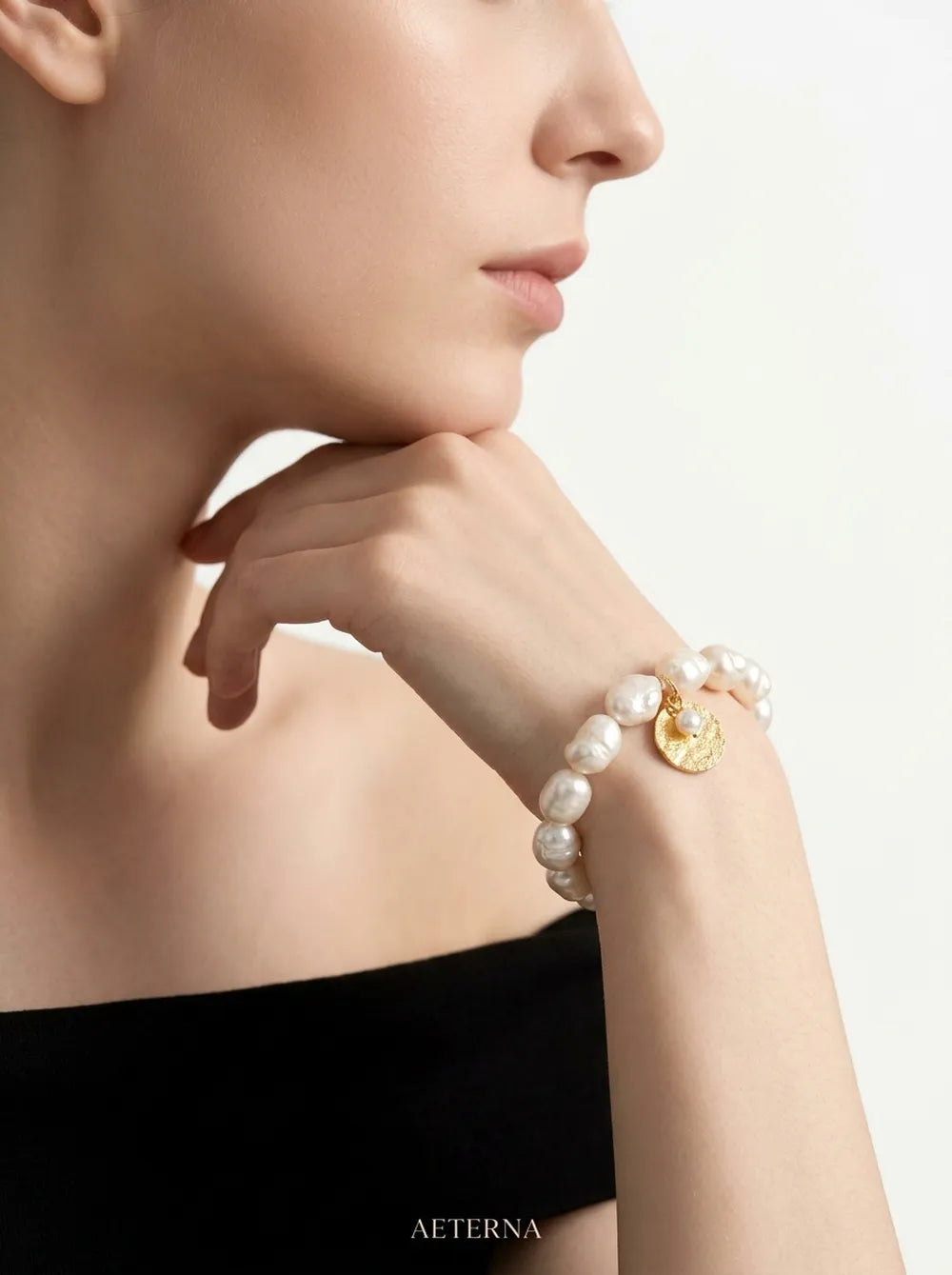 Profile shot of model in black off-shoulder top wearing the gardener pearl elastic bracelet.