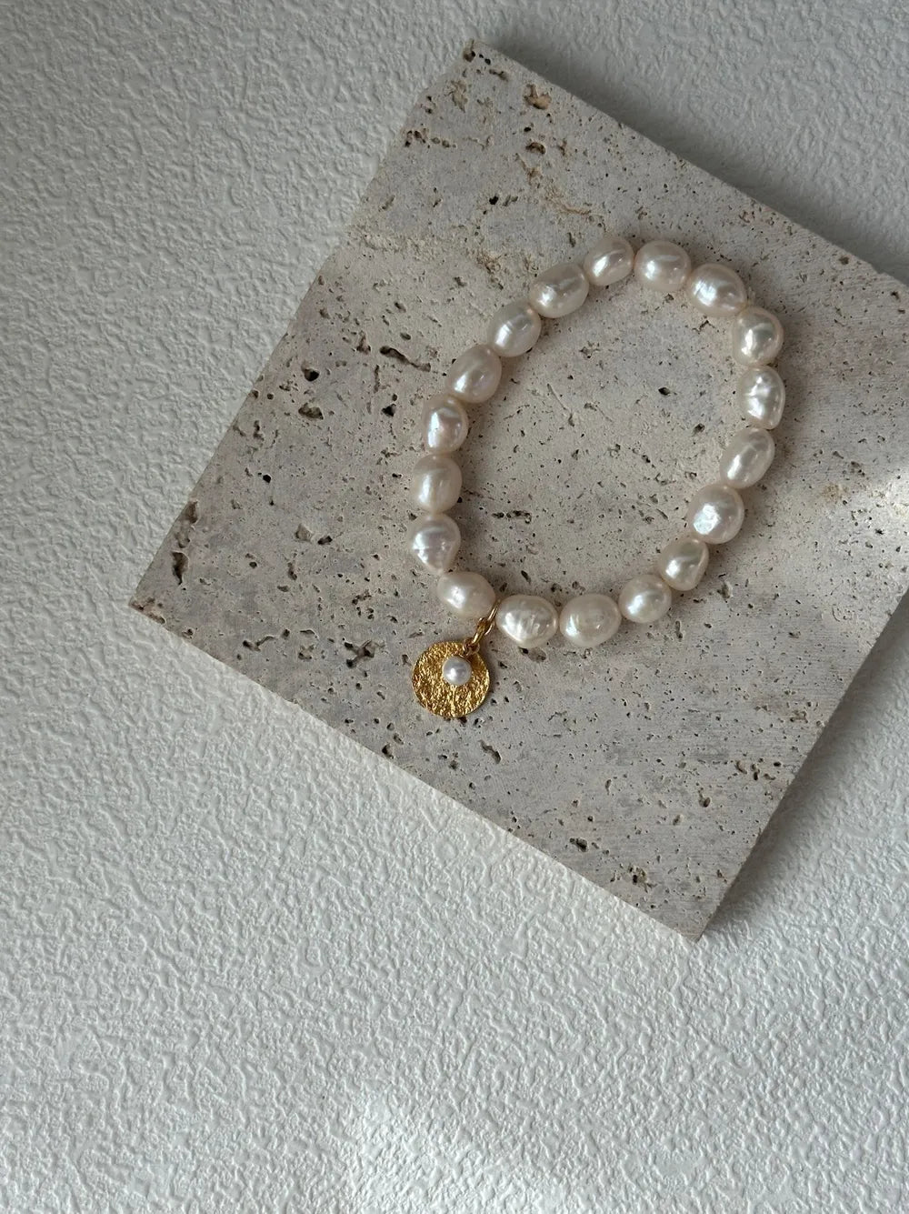Gardener freshwater pearl elastic bracelet with coin charm resting on square travertine tile.