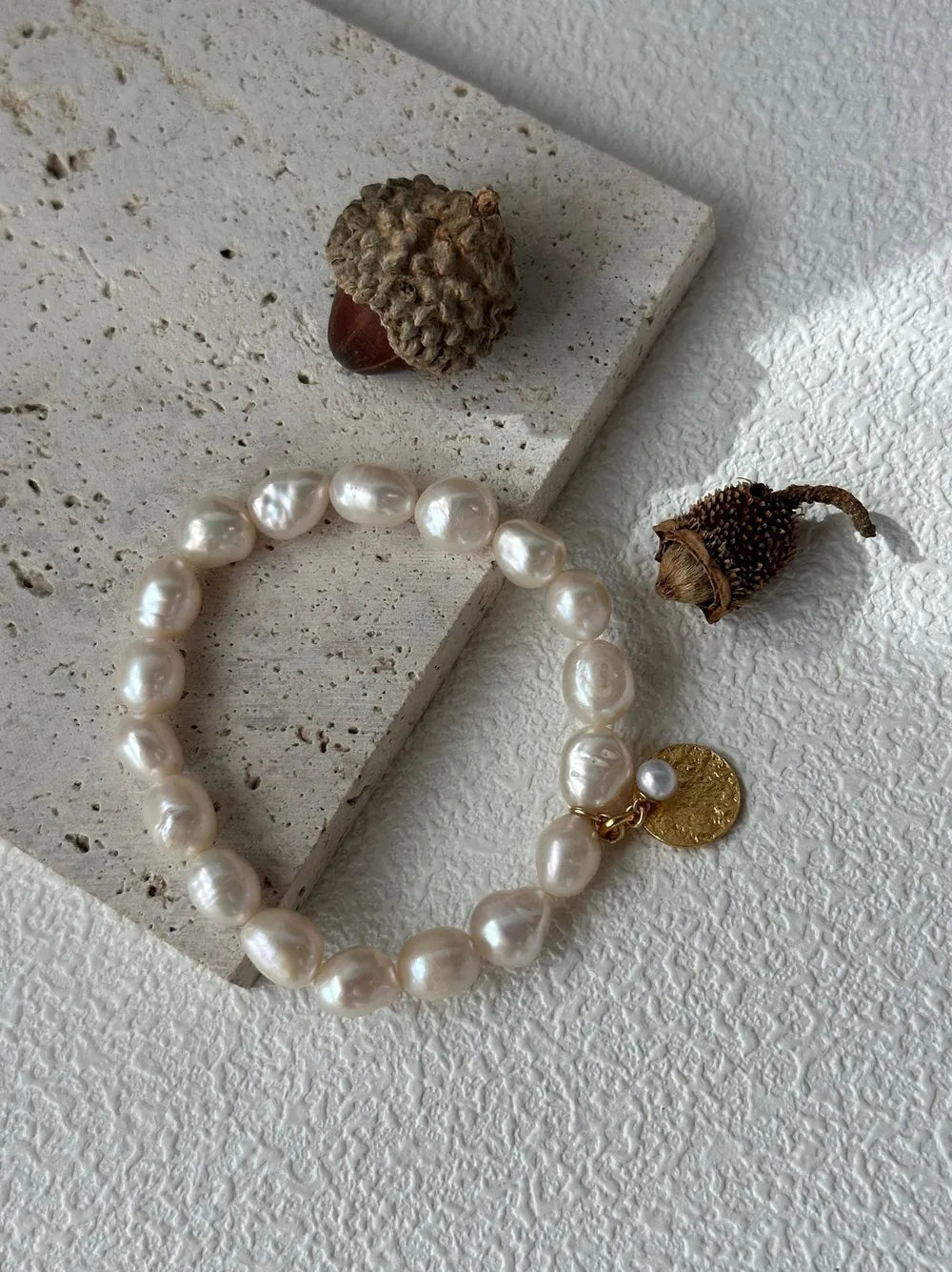 Gardener pearl elastic bracelet arranged on travertine stone slab with acorn photo props.