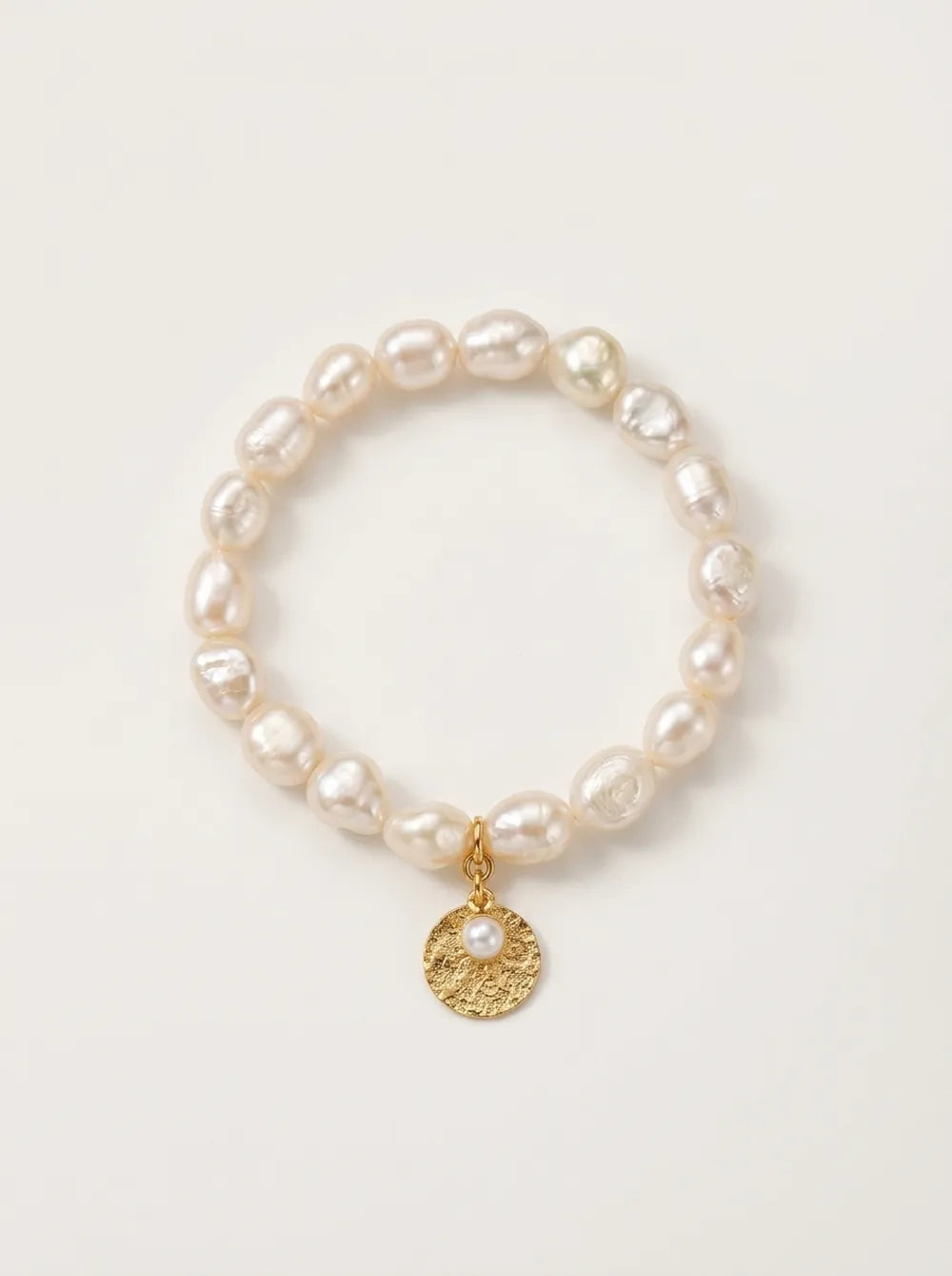 Flatlay view of the circular gardener freshwater pearl elastic bracelet with gold disk charm.