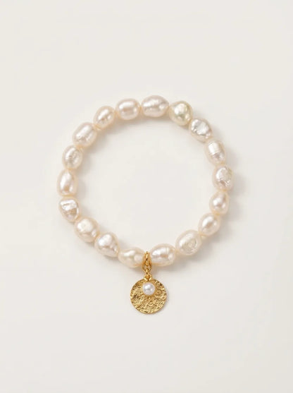 Flatlay view of the circular gardener freshwater pearl elastic bracelet with gold disk charm.