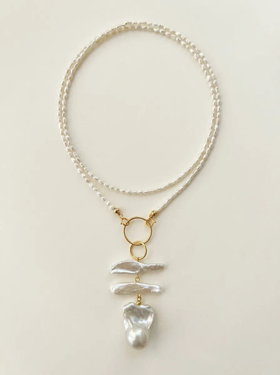 Full view of the geometric double ring baroque pearl long necklace on a neutral background.
