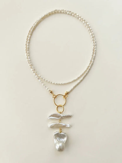 Full view of the geometric double ring baroque pearl long necklace on a neutral background.