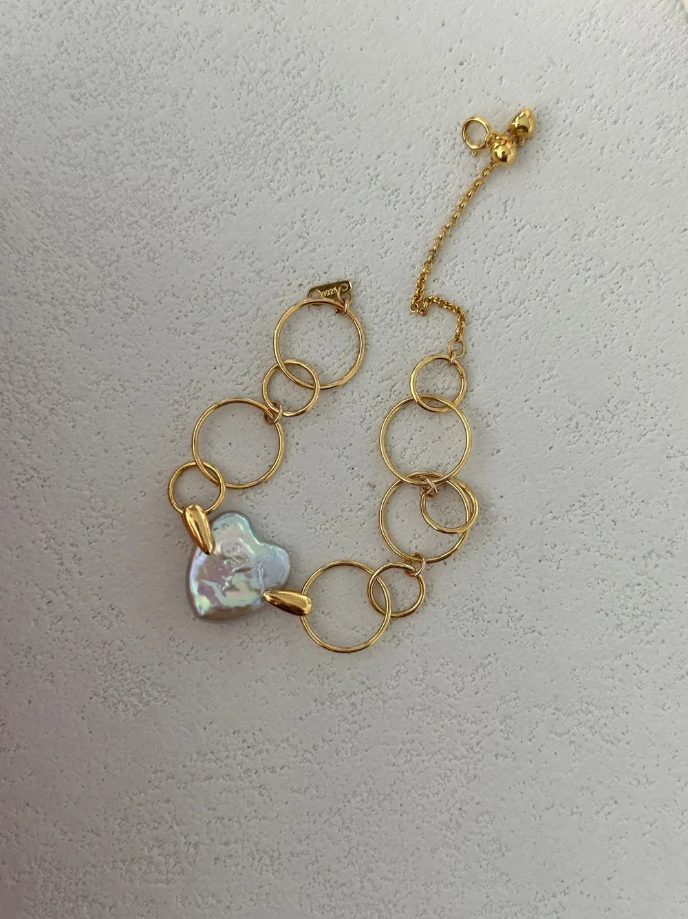 Overhead close-up shot highlighting the gold bead tag, clasp, and natural heart baroque pearl.