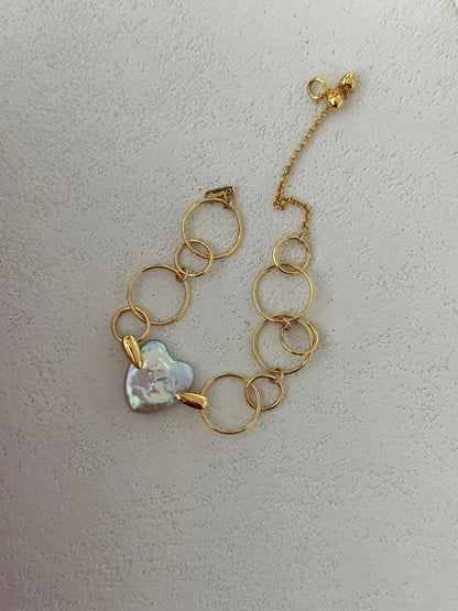 Overhead close-up shot highlighting the gold bead tag, clasp, and natural heart baroque pearl.