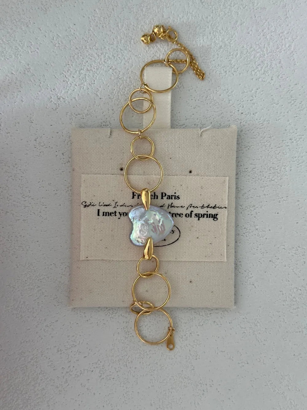 Geometric hoop heart baroque pearl bracelet displayed over a French printed linen pouch.