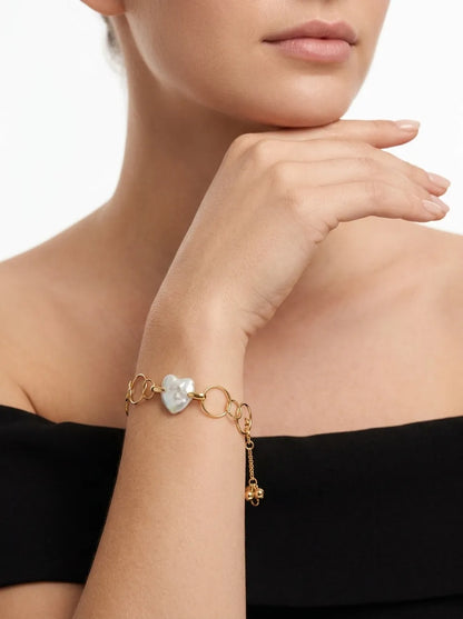 Model holding hand to chin displaying the geometric hoop heart baroque pearl bracelet on wrist.