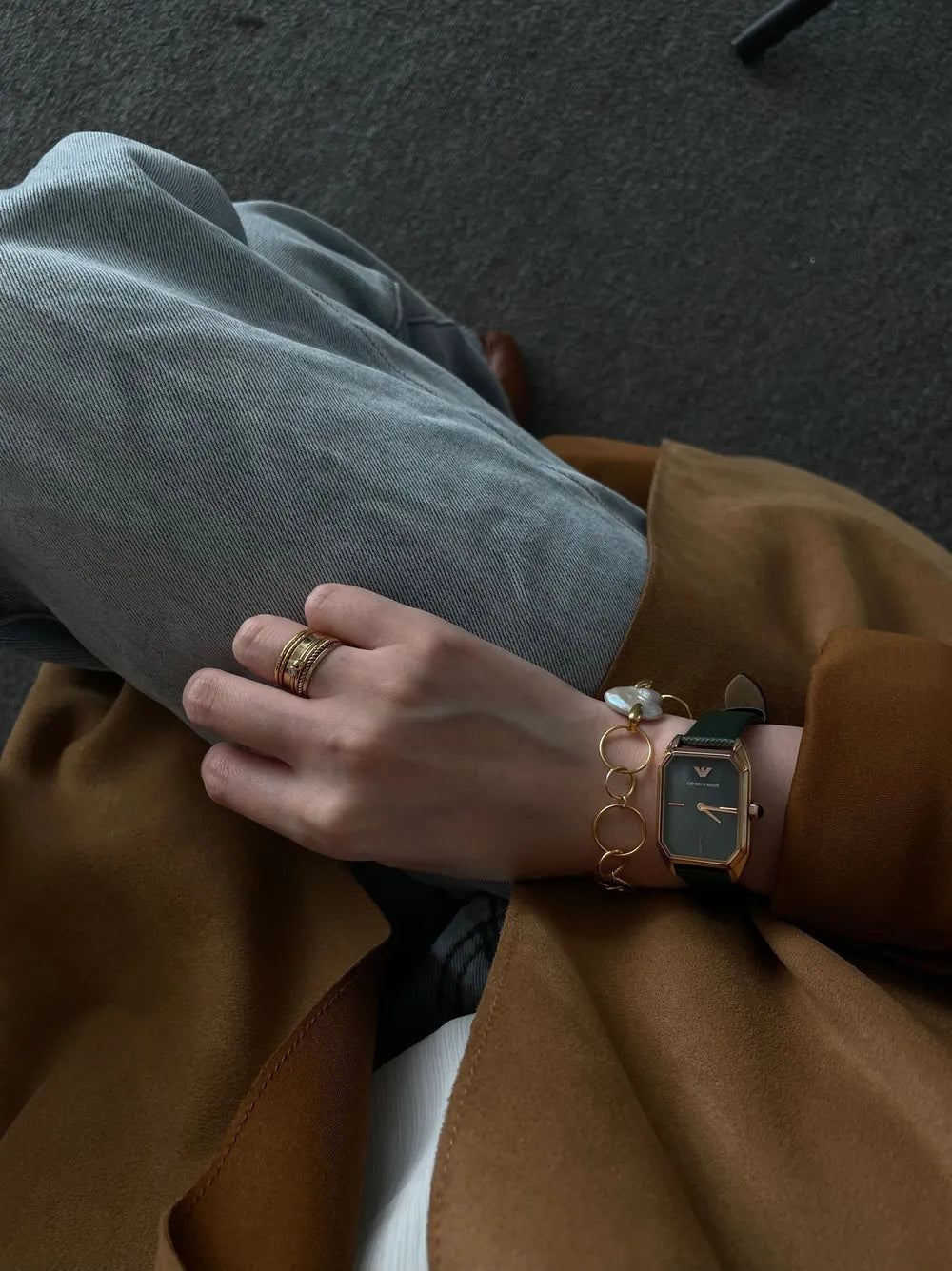 Seated model displaying the geometric hoop pearl bracelet paired with a gold square-dial watch.   