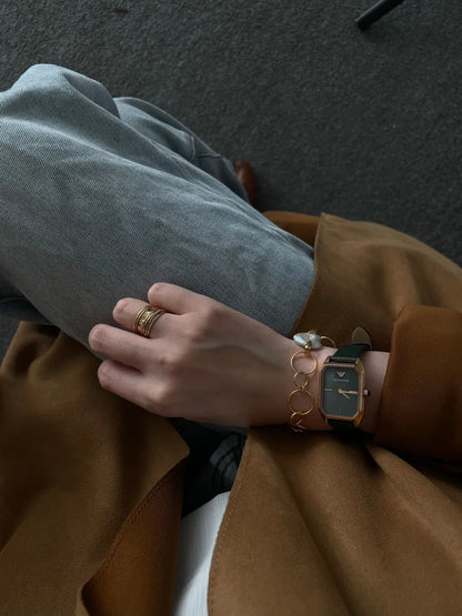 Seated model displaying the geometric hoop pearl bracelet paired with a gold square-dial watch.   