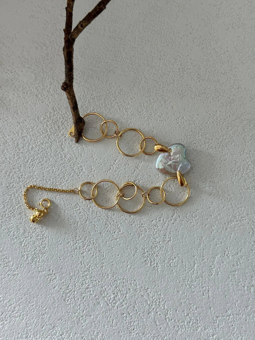 Geometric hoop heart baroque pearl bracelet draped near a tree branch prop.