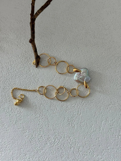 Geometric hoop heart baroque pearl bracelet draped near a tree branch prop.