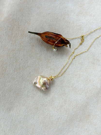 Natural rainbow baroque pearl displaying metallic luster next to dried botanical prop.