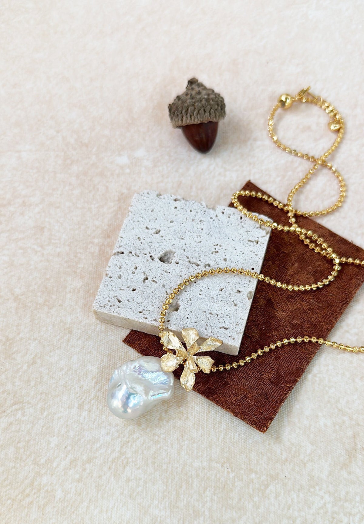 matte gold floral charm with irregular freshwater pearl, bridal jewelry on neutral beige background