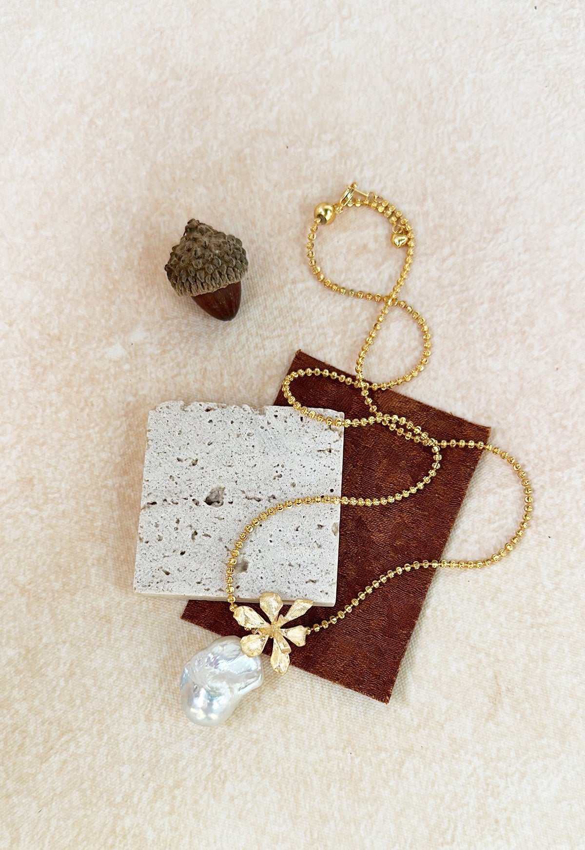 matte gold floral charm with irregular freshwater pearl, bridal jewelry on neutral beige background