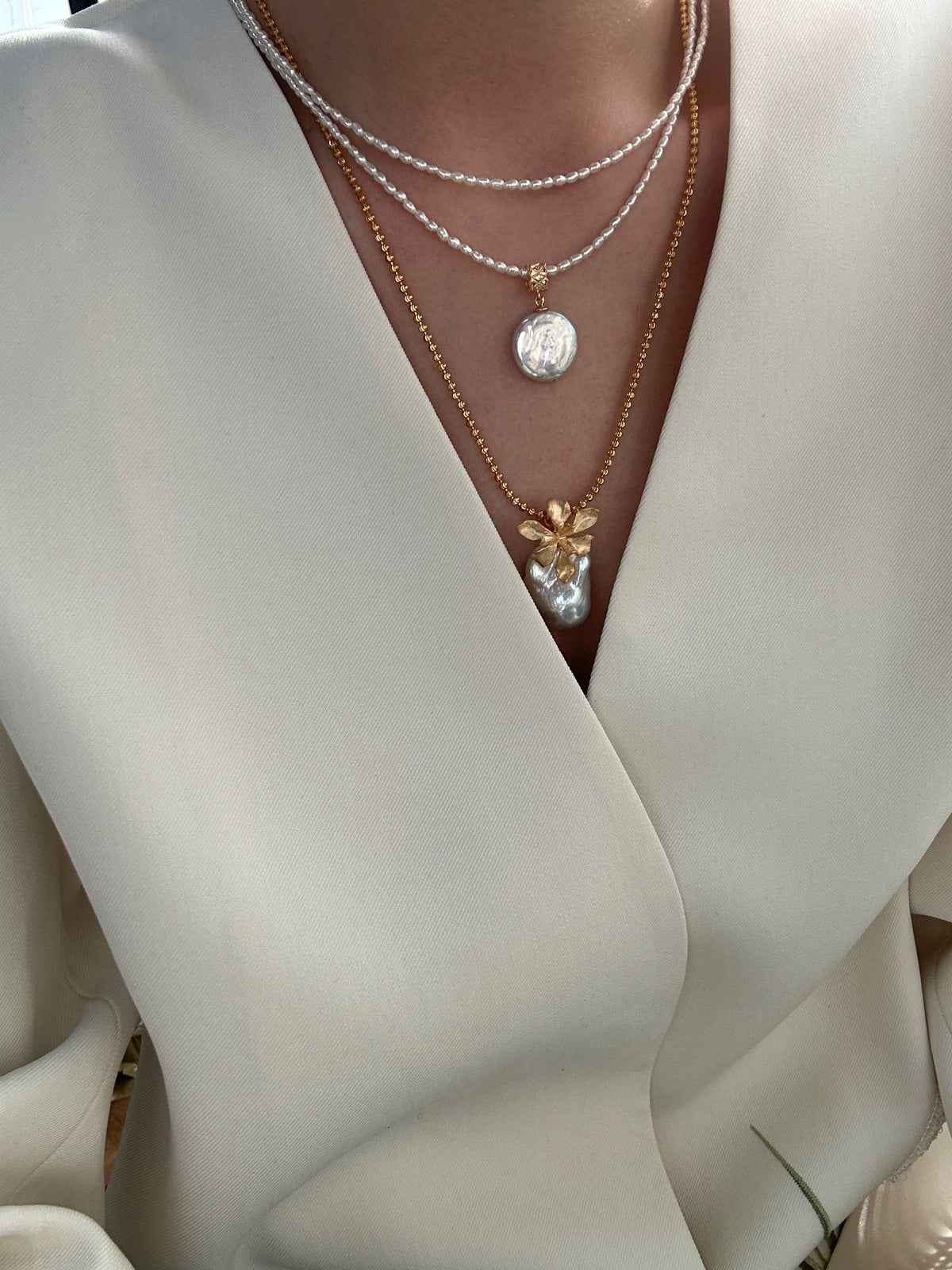 Model wearing layered pearl necklaces, matte gold flower baroque pearl pendant with cream wrap top, bridal outfit styling