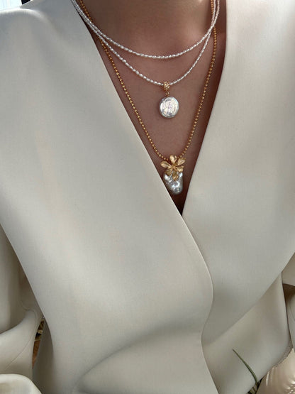 Model wearing layered pearl necklaces, matte gold flower baroque pearl pendant with cream wrap top, bridal outfit styling