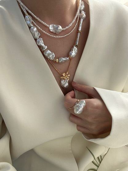 Model wearing layered pearl necklaces, matte gold flower baroque pearl pendant with cream wrap top, bridal outfit styling