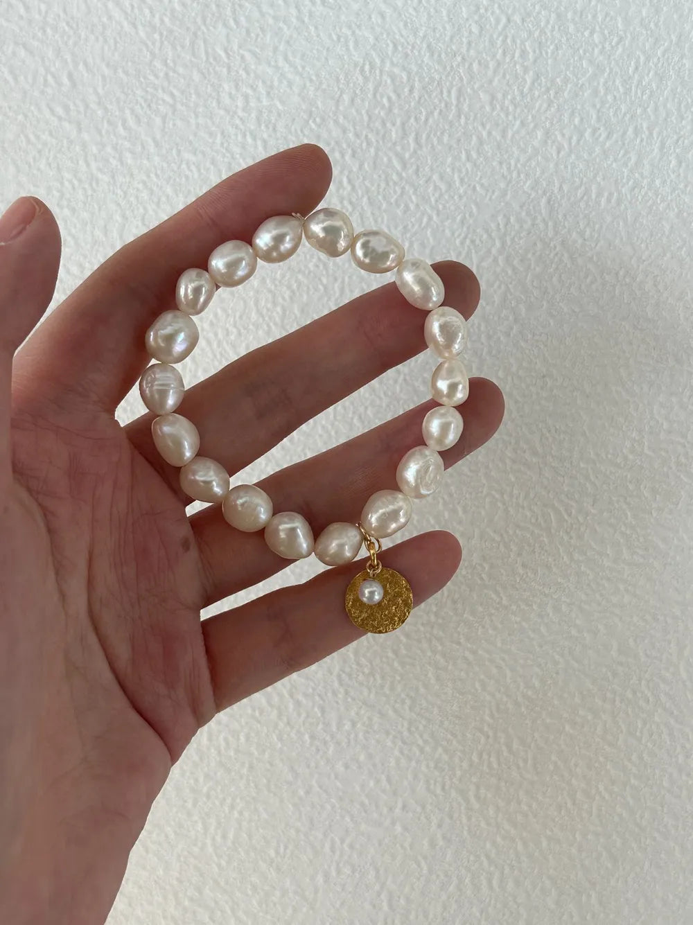 Hand displaying the gardener freshwater pearl elastic bracelet across palm under natural light.