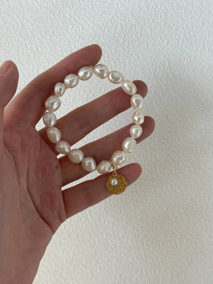 Hand displaying the gardener freshwater pearl elastic bracelet across palm under natural light.