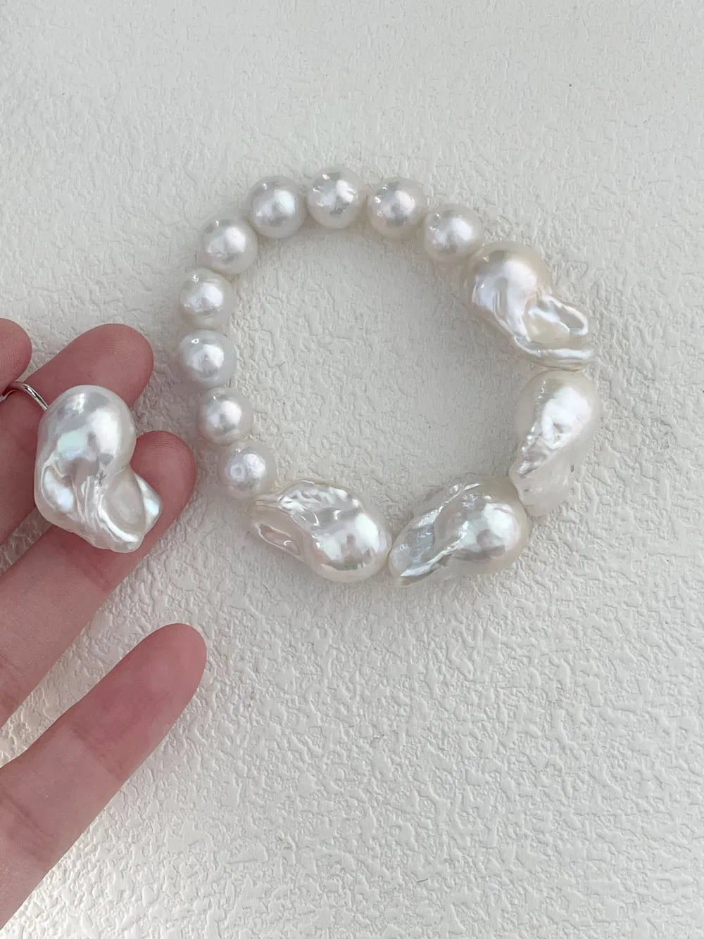 Hand holding the large baroque freshwater pearl beaded elastic bracelet demonstrating scale and luster.