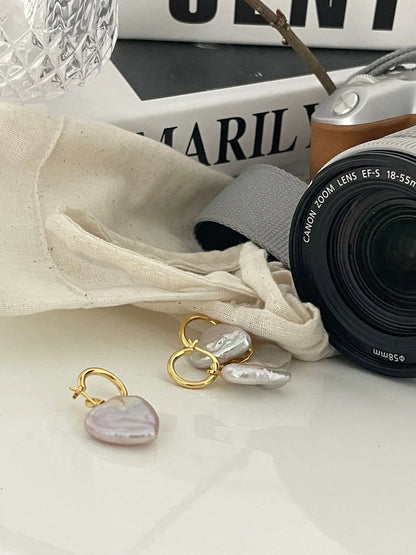 Large heart baroque pearl drop earrings displayed next to a vintage camera prop.