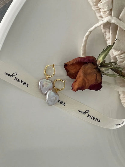 Heart-shaped baroque pearl hoop earrings arranged beside a dried red rose and ribbon prop.