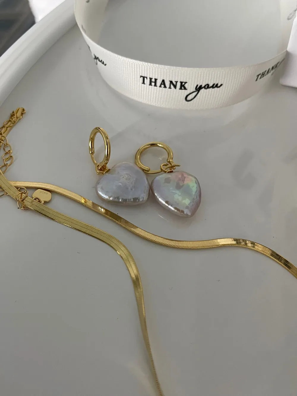 Heart baroque pearl earrings displayed with a gold snake chain on a white tray.