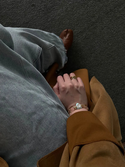 Model wearing jeans and camel coat holding the geometric hoop heart baroque pearl bracelet.