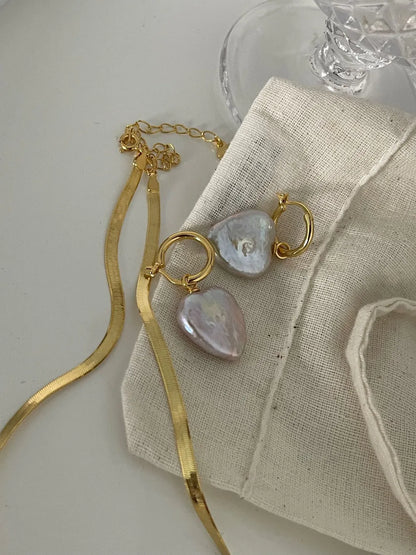 Heart baroque pearl huggie earrings styled with a gold herringbone chain on canvas pouch.
