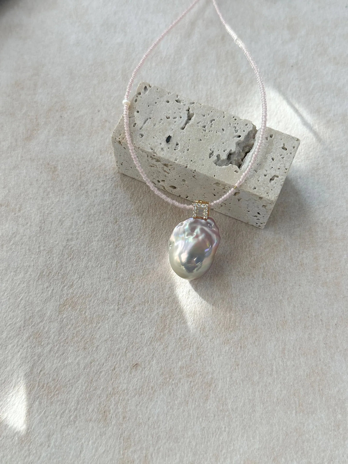Iridescent baroque pearl pendant on pink beaded strand displayed next to a stone prop.