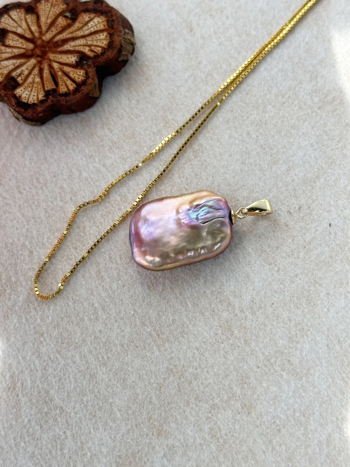 Macro shot showing rainbow luster of square baroque pearl and 18K gold-plated box chain.