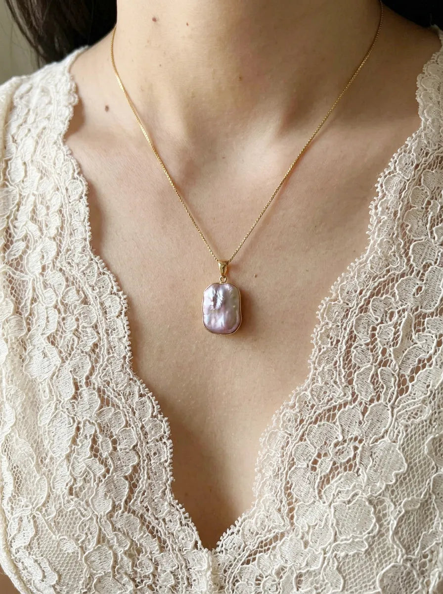 Model wearing iridescent square baroque pearl pendant necklace with cream lace dress.