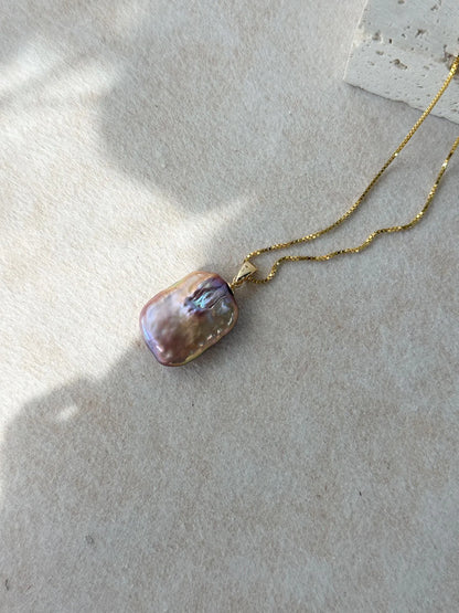 Iridescent purple-gold square baroque pearl pendant displayed against plaster prop.