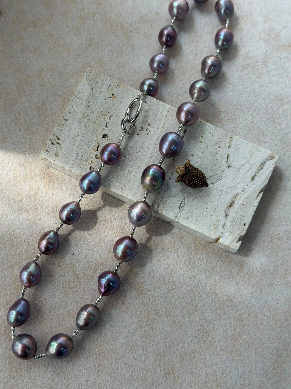 Angled display of iridescent violet baroque pearls with fine sterling silver chain link details.